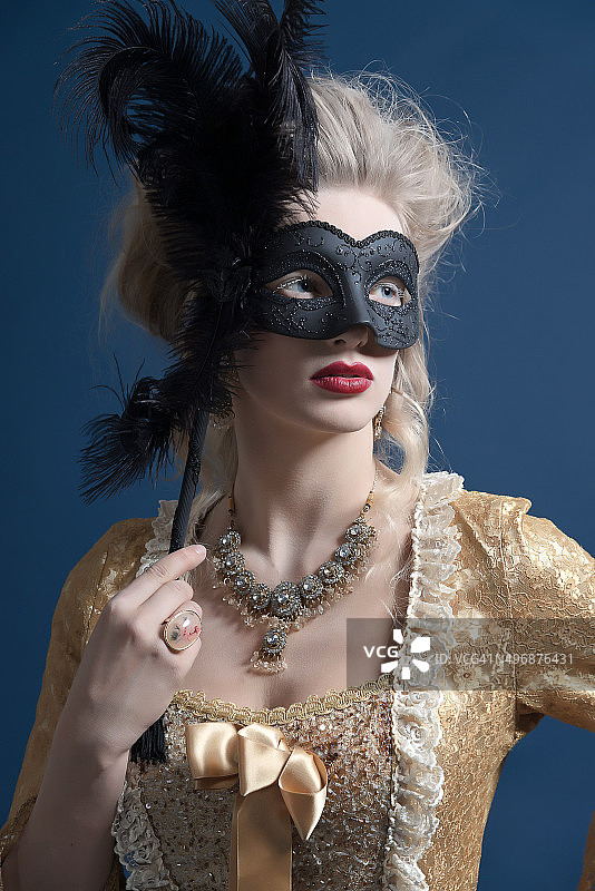 复古巴洛克时尚女性穿着金色连衣裙。拿着黑色的面罩。图片素材