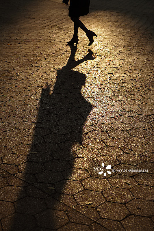 一个年轻女子的剪影独自行走在琥珀色的夕阳阴影中图片素材