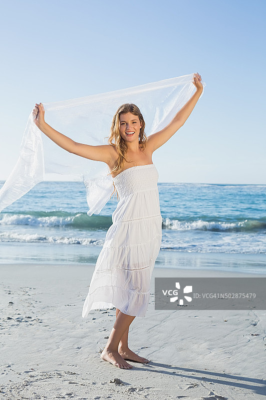 美丽快乐的金发碧眼在白色太阳裙与围巾的海滩上图片素材