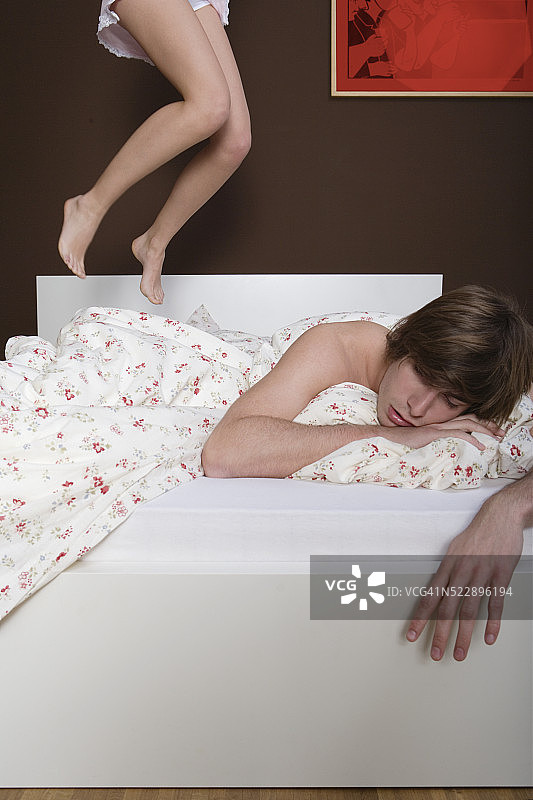 一个男人在睡觉，而他的女朋友正在床上跳图片素材