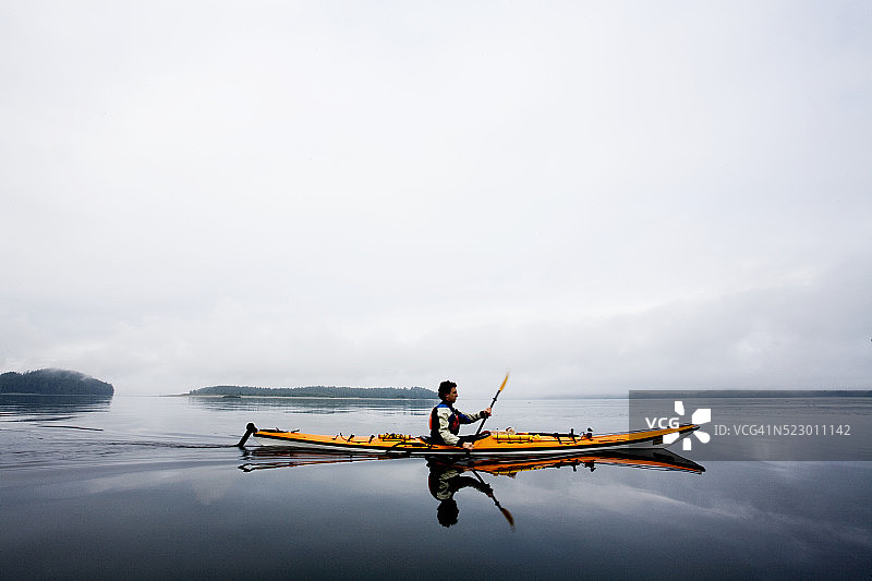 男子皮划艇在阴天平静的水图片素材