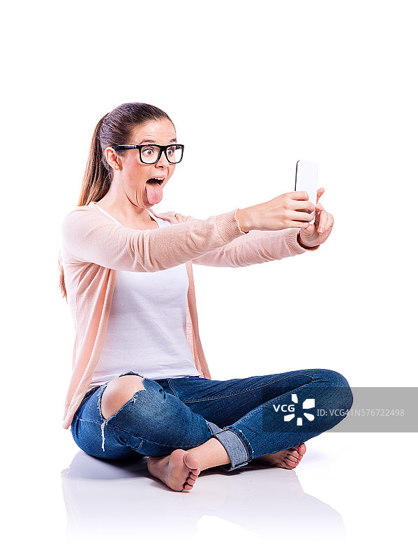 一个拿着智能手机的女人坐在地板上，被拍摄，孤立图片素材