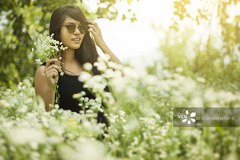 美丽的亚洲女孩的肖像在草地上拿着野花。图片素材