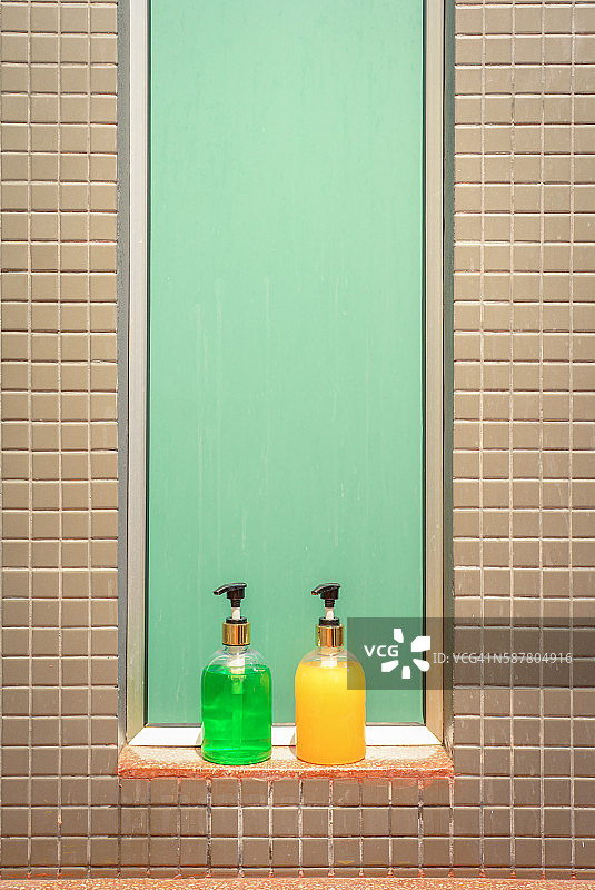 贴着瓷砖的墙上装着绿色和黄色的肥皂和洗发水图片素材