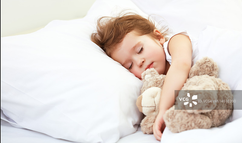 小女孩和泰迪熊睡在床上图片素材