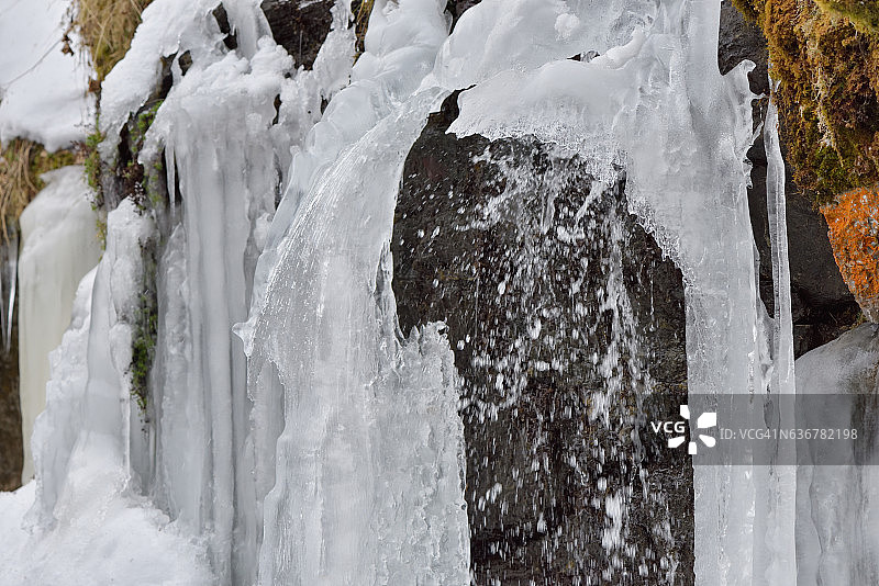 在寒冷的冬天，冰柱挂在山上的岩石上图片素材