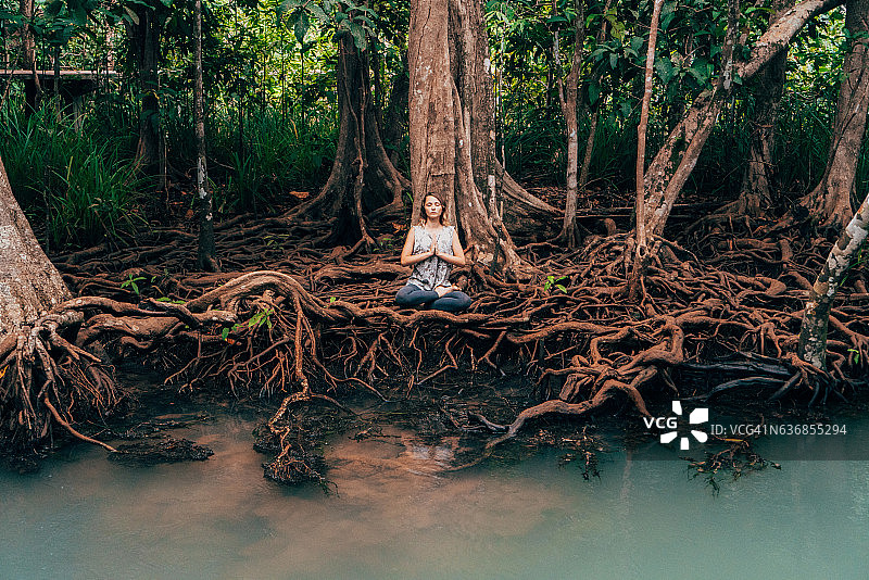 在热带森林的河边做瑜伽的女人图片素材