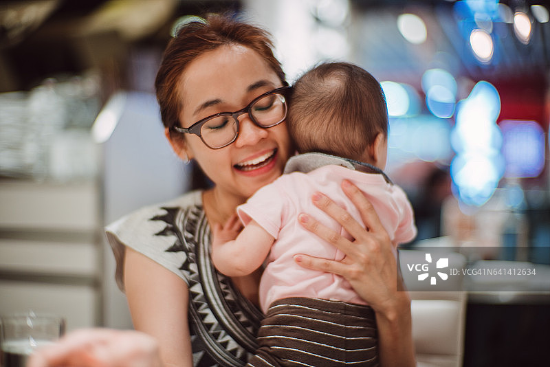 年轻漂亮的妈妈在餐馆里快乐地拥抱着宝宝图片素材