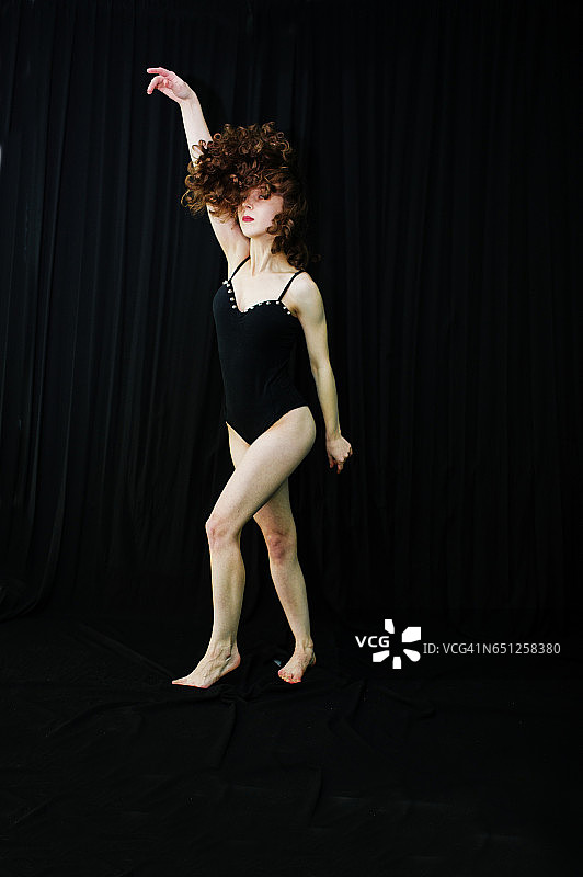 女舞者在黑色的背景上蹦蹦跳跳。摄影棚里的女人在跳舞。图片素材