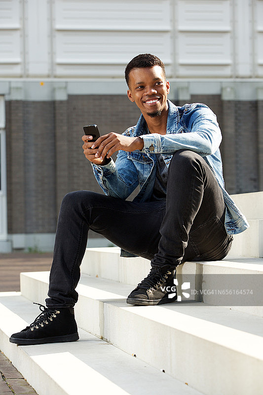 快乐的非洲人坐在外面的台阶上拿着智能手机图片素材