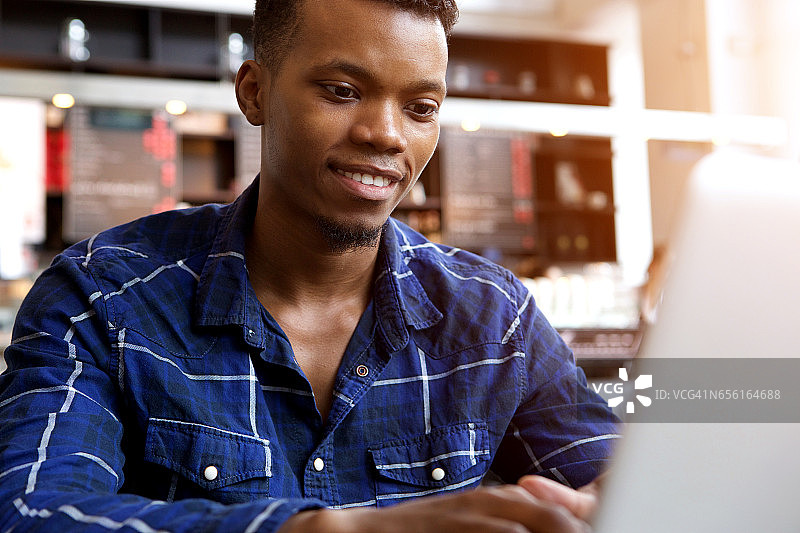微笑的年轻人坐在咖啡馆里用笔记本电脑工作图片素材