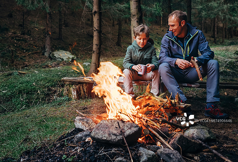 父亲和儿子在篝火旁取暖，喝茶聊天图片素材
