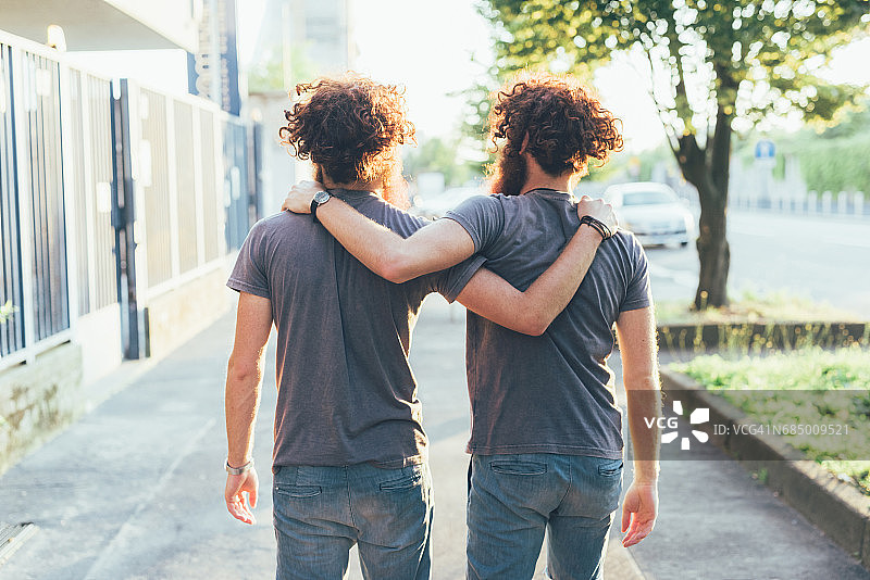 一模一样的成年男性双胞胎在人行道上散步的后视图图片素材