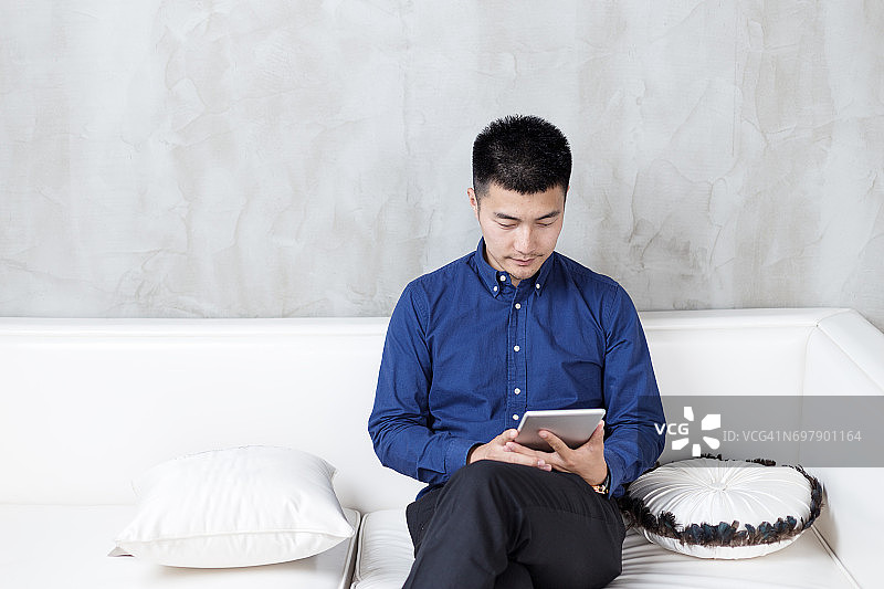 年轻的亚洲男人在沙发上放着平板电脑图片素材