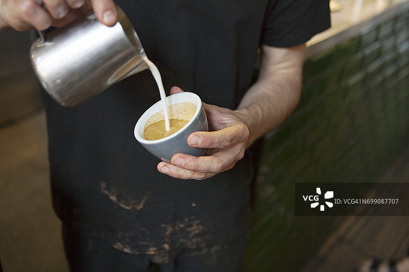 咖啡馆里，男咖啡师的手正在往咖啡杯里倒牛奶图片素材