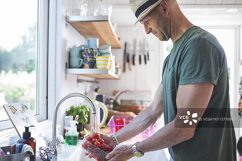 男人在厨房水龙头下清洗樱桃番茄的侧视图图片素材