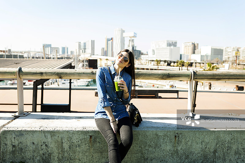 西班牙，巴塞罗那，微笑的年轻女子喝着饮料享受阳光图片素材