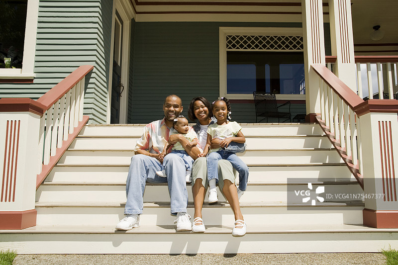 一个年轻的家庭坐在他们房子前的台阶上。图片素材