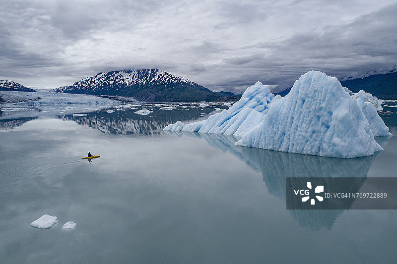 美国阿拉斯加州，帕尔默，乔治湖，在多云的天空下的冰山旁划独木舟的人图片素材