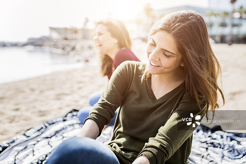 两个快乐的年轻女人坐在海滩上图片素材