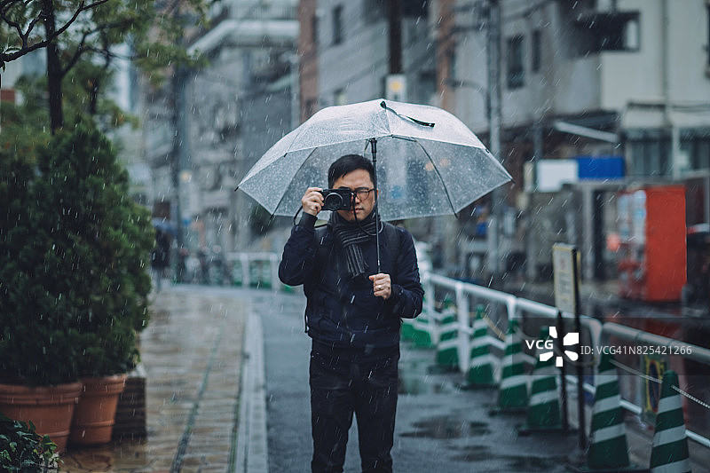 一名年轻人带着雨伞在冬天下雪时用相机拍照图片素材