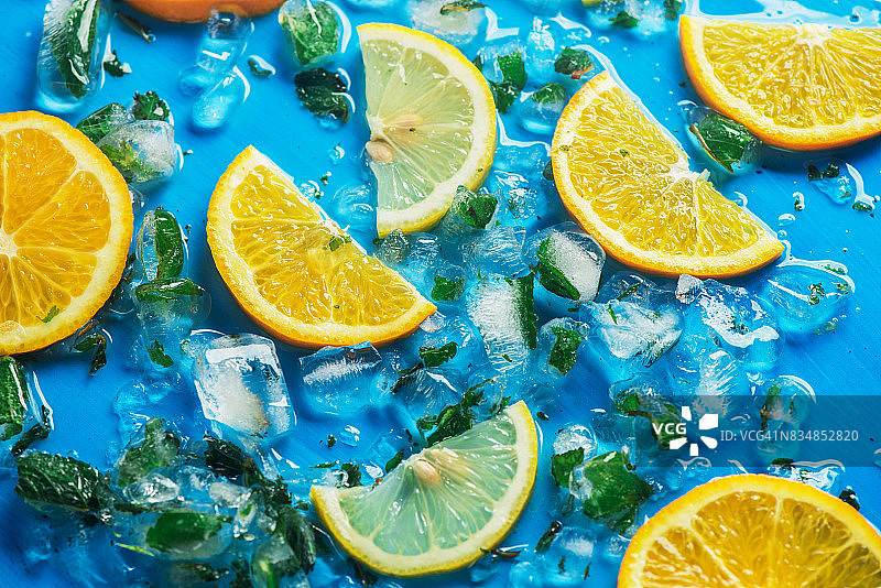 在蓝色背景和冰块上的橙子和柠檬片的特写图片素材