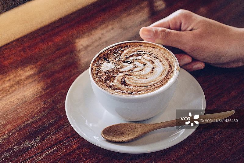 人类手握一杯热卡布奇诺咖啡的镜头。图片素材