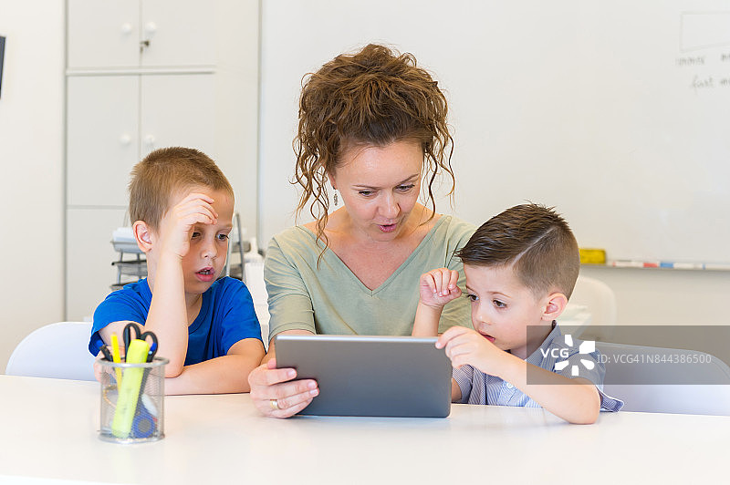 一名女教师和两个学龄前的男孩在教室里使用平板电脑图片素材
