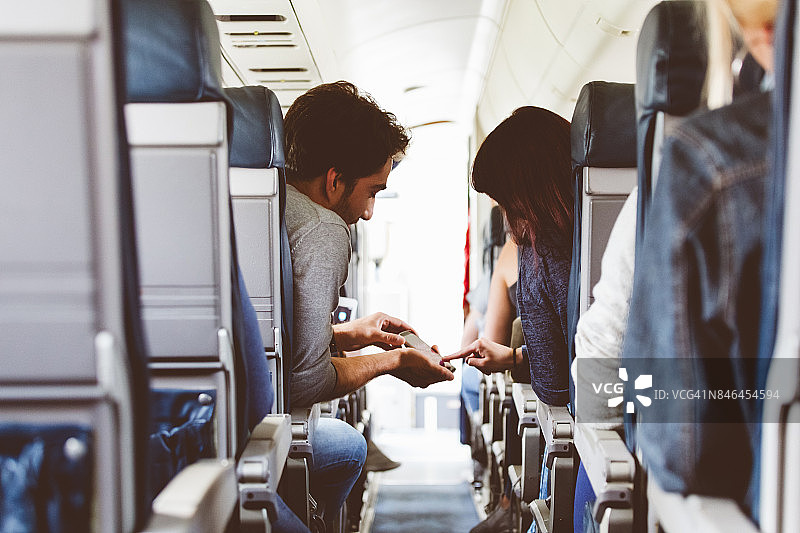 一对年轻夫妇在飞机上使用手机图片素材