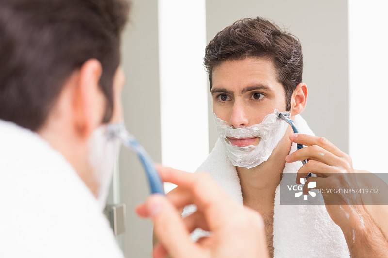 一个年轻人在浴室里用反光刮胡子图片素材