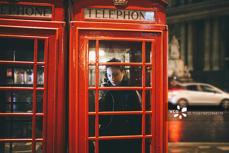 一位年轻女子在伦敦的公共电话亭里打电话图片素材