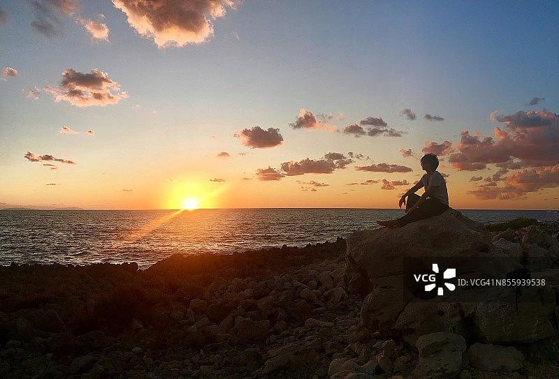 西西里北部，一个女人坐在岩石上看日落图片素材