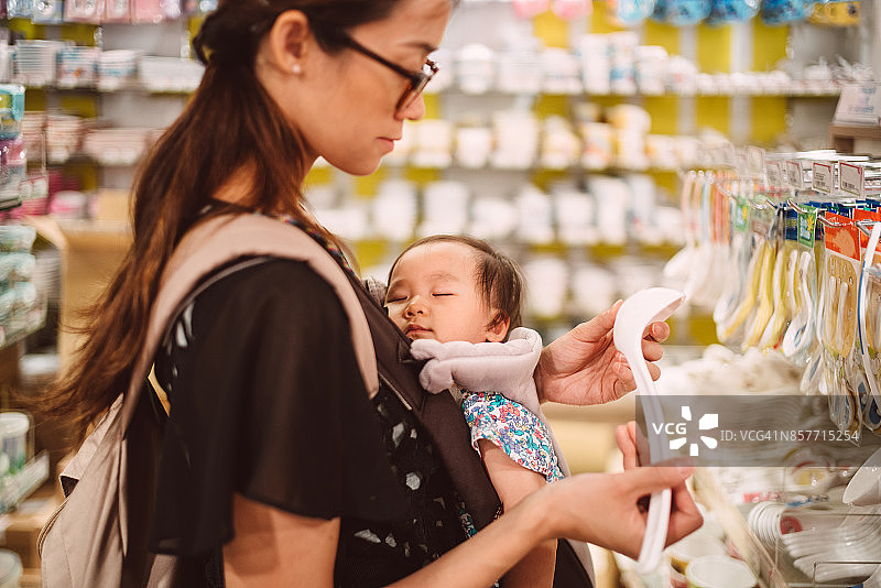 年轻漂亮的妈妈抱着熟睡中的婴儿在百货商店买家庭用品。图片素材