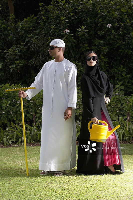 阿拉伯夫妇拿着干草叉和喷壶在花园里。图片素材