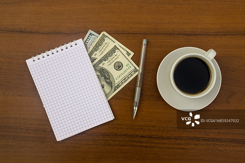 一杯咖啡，美元，笔记本和笔放在木桌上图片素材