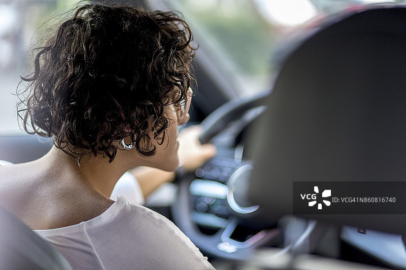 年轻女子坐在一辆黑色轿车的驾驶座上，开车。图片素材