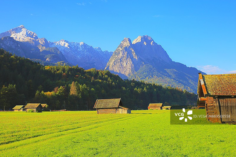 阿尔卑斯乡村木谷仓农场，与Zugspitze, Waxenstein和Alpspitze景观-戏剧性的景观在巴伐利亚阿尔卑斯山，德国，附近的卡文德尔山脉-雄伟的高山景观秋天-加尔米施，德国巴伐利亚图片素材