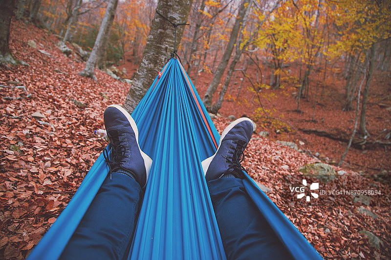 在蒙特塞尼山旅行期间，盖伊在美丽的森林里享受秋天，在一个独特的地方，他在一个自然之间摇摆的吊床上休息，凝视着美丽的树木。图片素材