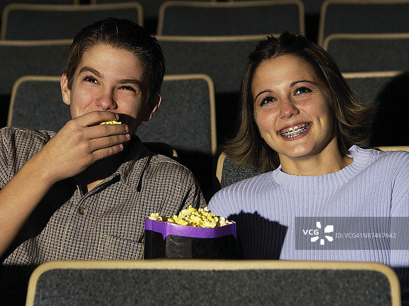 一个年轻的白人青年夫妇坐在电影院吃爆米花和享受电影的特写图片素材