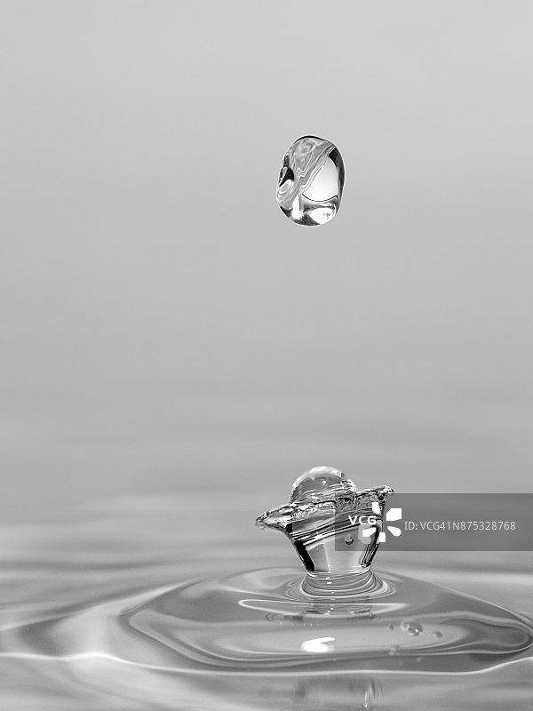 一组水滴悬在空中，落在水面上，形成图形和抽象的形式，在灰色的背景图片素材