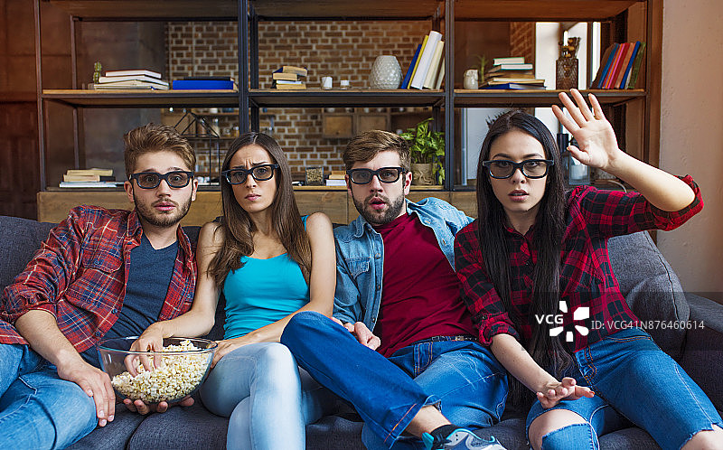 一群年轻的朋友戴着3d眼镜坐在沙发上吃着爆米花看电影图片素材