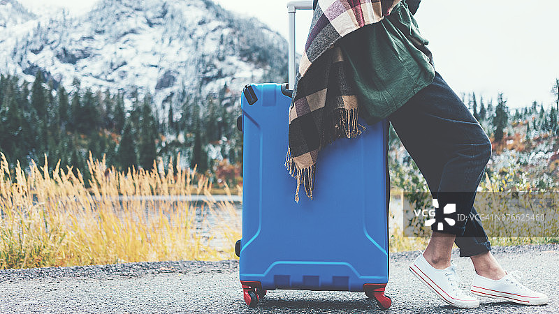 一个旅行中的女人坐在她的蓝色行李箱上，旁边是野生的风景图片素材