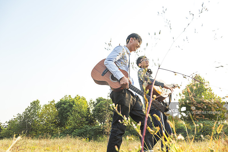 两个男人，朋友，在日落的时候在草坪上弹着吉他图片素材
