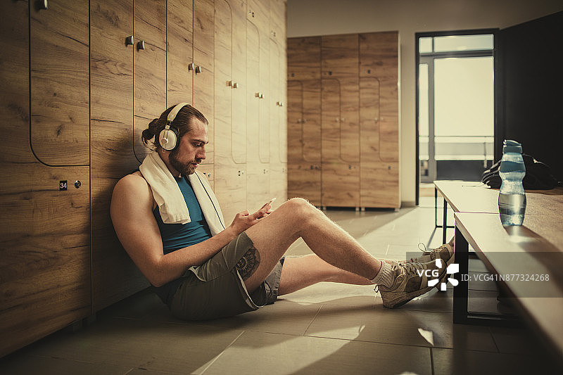 运动员戴着耳机听音乐，运动训练后在更衣室休息。图片素材