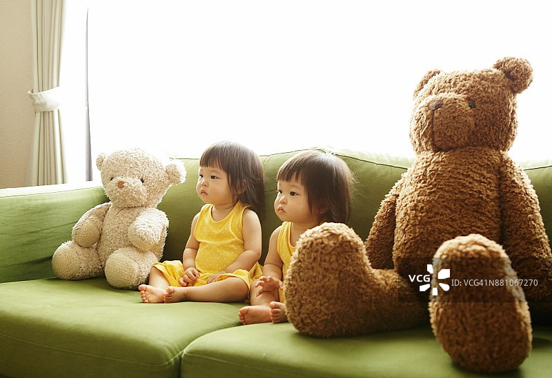 双胞胎妹妹和泰迪熊坐在沙发上图片素材
