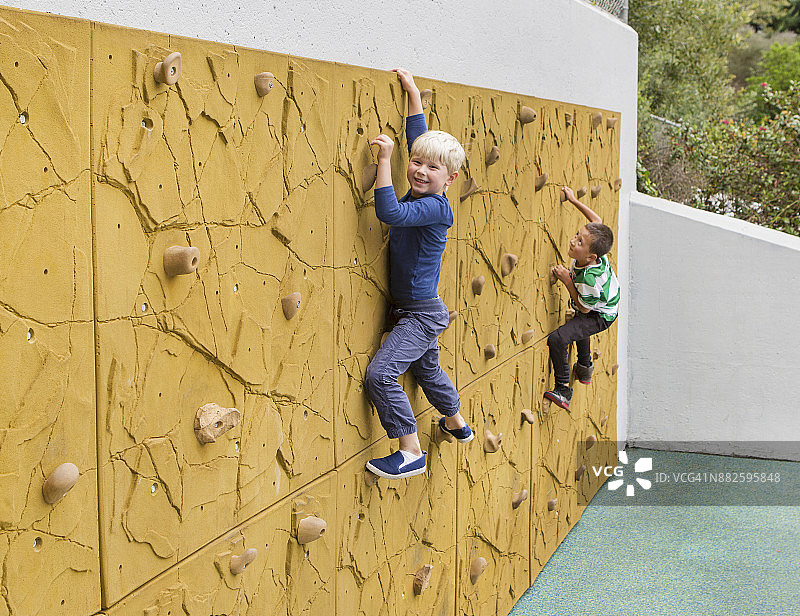 两个男孩(6-7岁)正在攀爬攀岩墙。图片素材