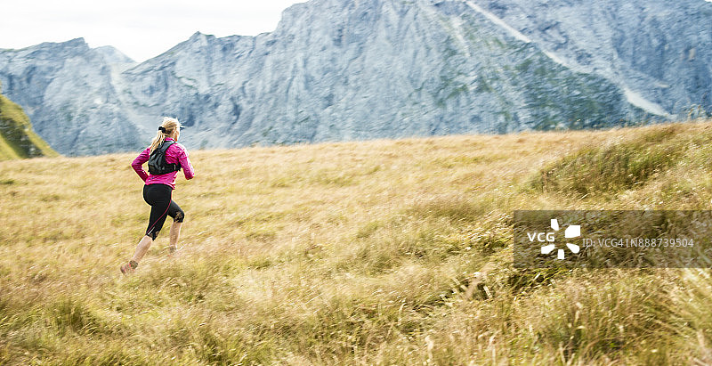 女跑步者穿过高山上的草地图片素材