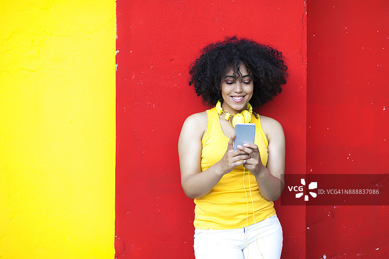 漂亮的非洲女人戴着黄色耳机和智能手机图片素材