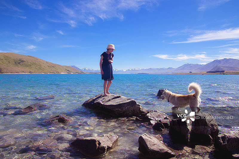 一个女孩站在特卡波湖的岩石上，水中有一只哈士奇狗图片素材