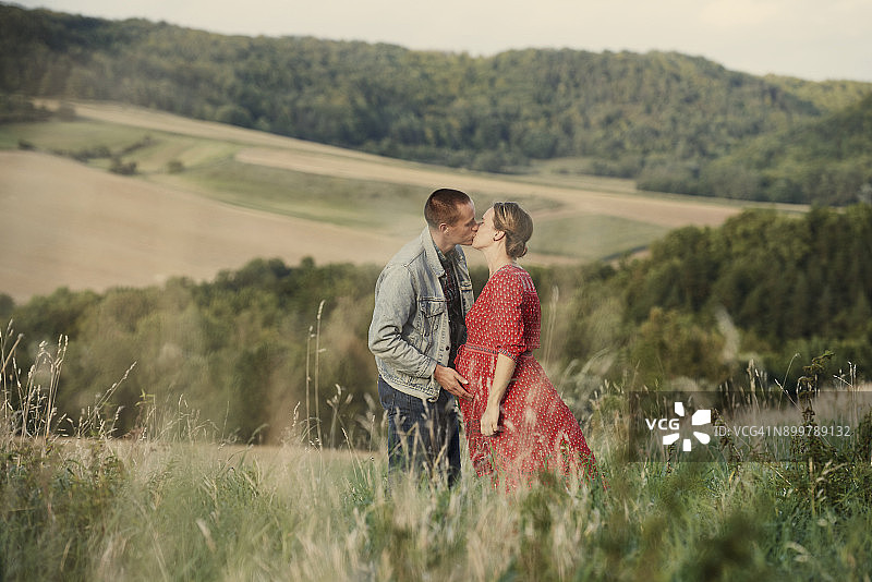 浪漫的怀孕中年夫妇在田野亲吻图片素材